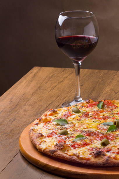 pizza marguerita made with tasty pizza dough, mozzarella, tomatoes, marjoram and green olives. served on a wooden board. napolitan pizza. red wine served in a crystal glass. - crystal noodles imagens e fotografias de stock