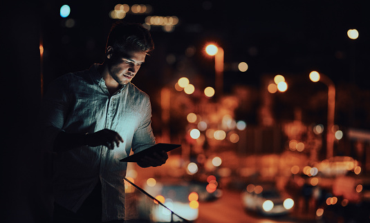 Shot of a young businessman using a digital tablet outside an office at night