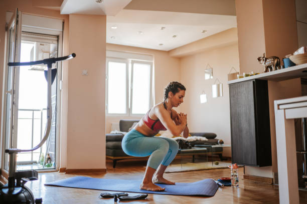 Home exercising Young woman doing home workout in living room squatting position photos stock pictures, royalty-free photos & images