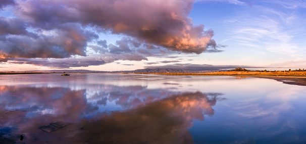 Sunset views of the restored wetlands of South San Francisco Bay Area, with dark clouds reflected on the water surface and Diablo Mountain Range visible in the background, Mountain View, California
