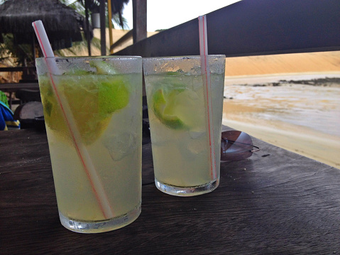 Two caipirinhas on a table overlooking the baech.