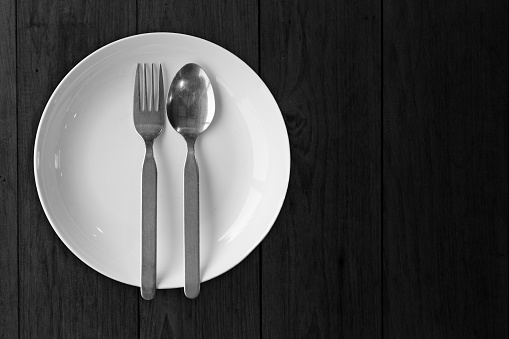 White dish plate with fork spoon on black wooden blank empty no food image for decoration.