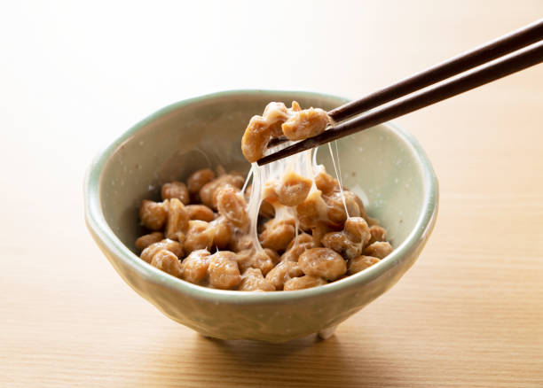 Natto placed on a wooden background Natto in a plate set against a wooden background is lifted with chopsticks natto stock pictures, royalty-free photos & images