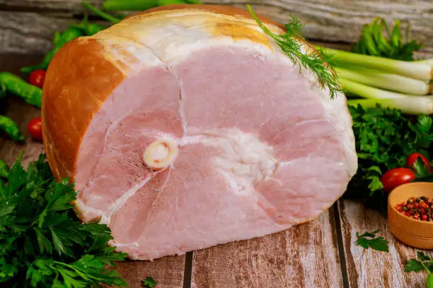 Smoked bone in ham with vegetables and spice on wooden Christmas table. Close up.