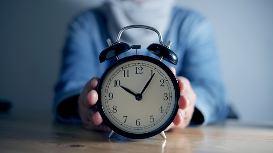 Woman holding alarm clock, time management concept, selective focus on clock with blurry person