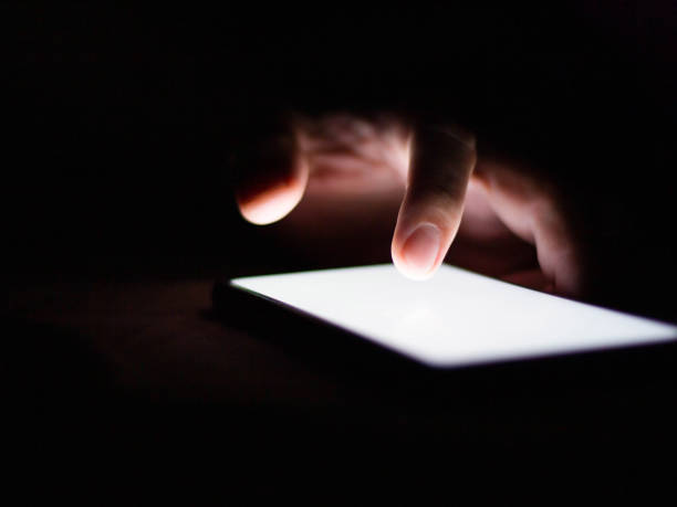istock Man using a smartphone in the dark navigating the glowing blue touchscreen with his finger. 1240968271