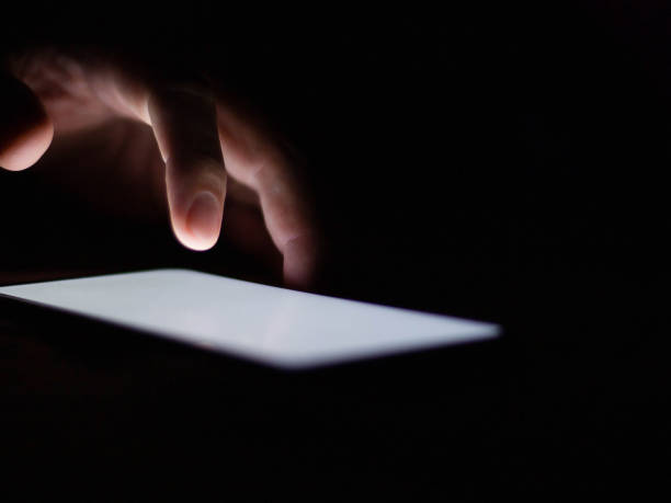istock Man using a smartphone in the dark navigating the glowing blue touchscreen with his finger. 1240968311