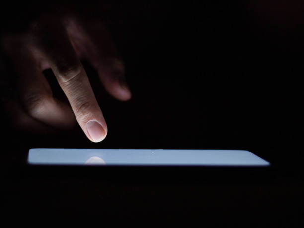 istock Man using a smartphone in the dark navigating the glowing blue touchscreen with his finger. 1240968312