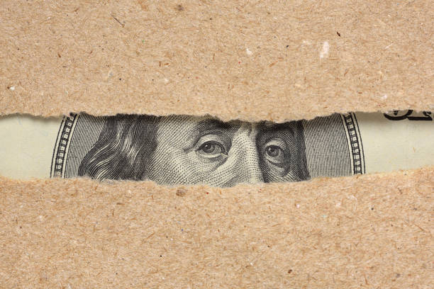 One hundred dollar bill behind brown craft ripped paper One hundred dollar bill Benjamin Franklin portrait looks behind brown craft ripped paper hiding stock pictures, royalty-free photos & images