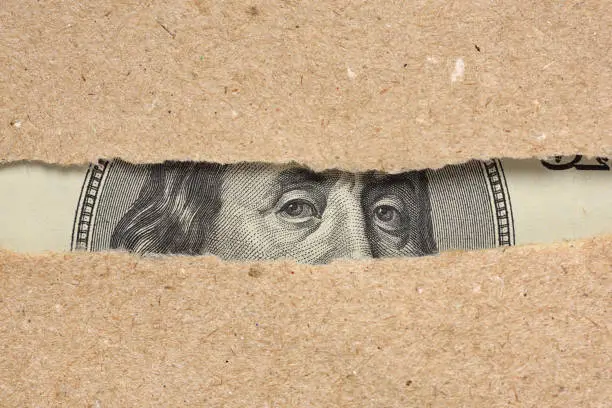 Photo of One hundred dollar bill behind brown craft ripped paper