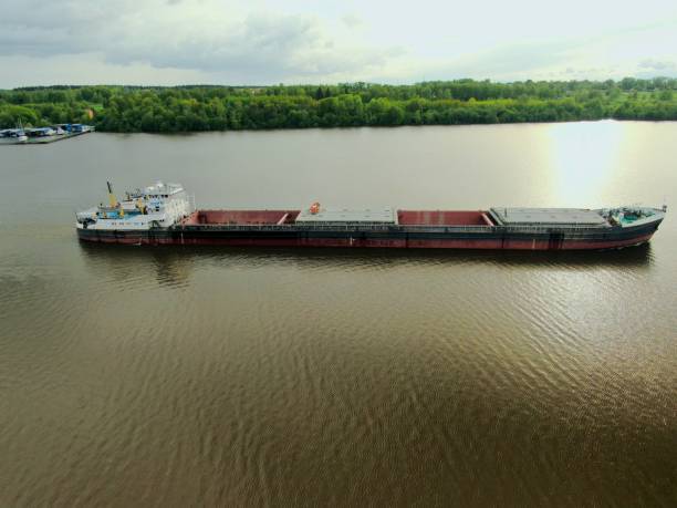 istock Flying over a large cargo ship with open holds sailing down a calm river surrounded by forest. Carriage of goods by river. Beautiful panoramic landscape. Top view down 1241023460
