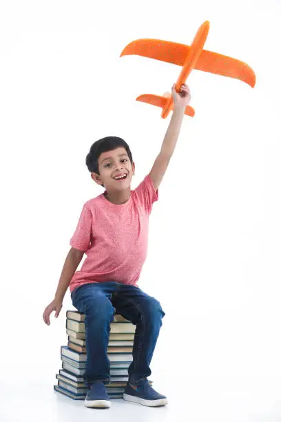 Indian, Asian child boy sitting on books and playing with plane model thinking high and smiling