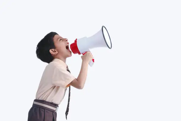 Indian, Asian Child Boy Student Shouting Through Megaphone on White Backdrop with Available Copy Space. Back to School Concept.
