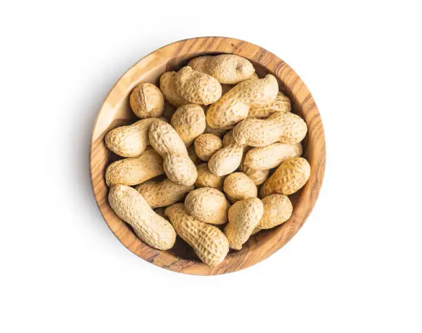 Tasty unpeeled peanuts in bowl isolated on white background.