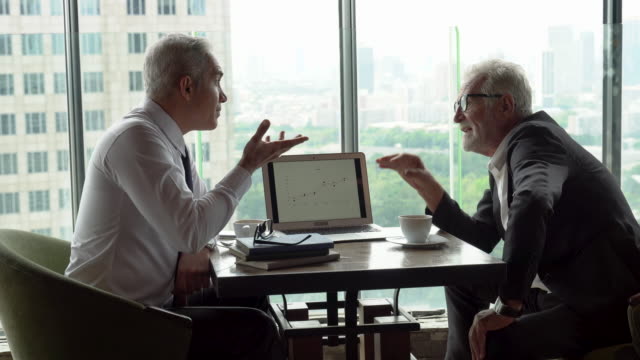 two senior management businessman debating  in meeting with data information in laptop. old man ceo discussing with client in cafe. serious mature manager talking by window over cityscape hi class