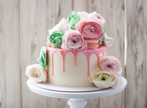 White cake with pink melted chocolate, meringues, macaroons and fresh flowers. Rustic background.