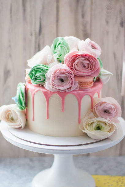 istock White cake with pink melted chocolate, meringues, macaroons and fresh flowers. Rustic background. 1241134532