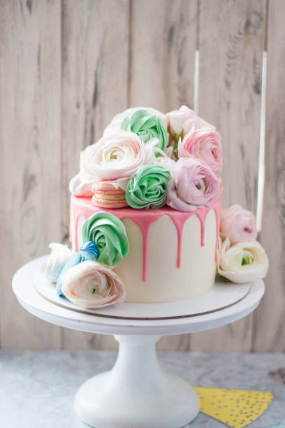 istock White cake with pink melted chocolate, meringues, macaroons and fresh flowers. Rustic background. 1241134533