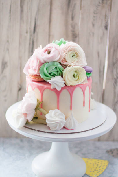 istock White cake with pink melted chocolate, meringues, macaroons and fresh flowers. Rustic background. 1241134550