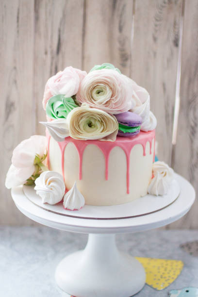 istock White cake with pink melted chocolate, meringues, macaroons and fresh flowers. Rustic background. 1241134556