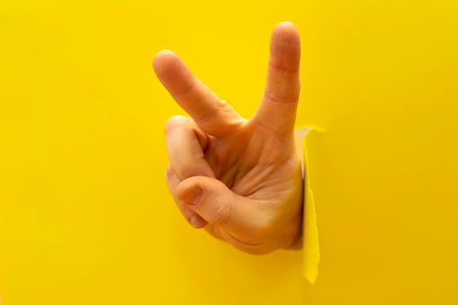 a hand from a hole in a paper wall shows the sign of Victoria on yellow background