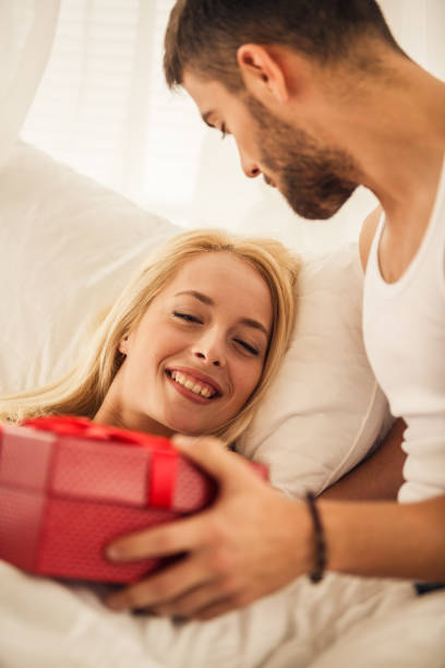 istock Young man surprising his loving girlfriend with a gift in bed 1241165196