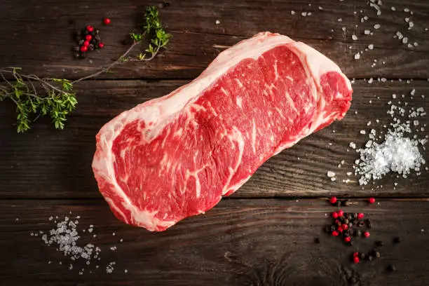 Photo of raw strip loin steak on white wooden background in rustic style