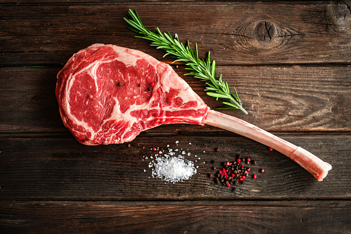 raw Tomahawk steak on wooden background with spices for grilling