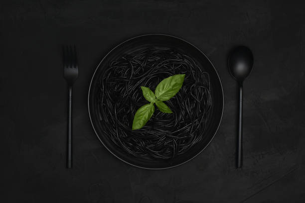 istock Black spaghetti in plate decorated with basil on black background. 1241192786