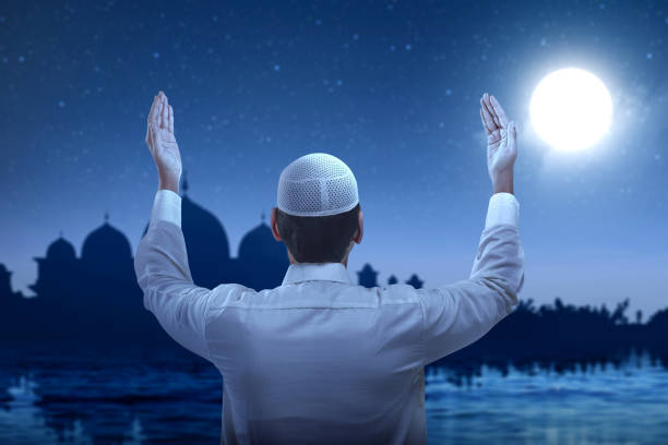 Rear view of Asian Muslim man standing while raised hands and praying Rear view of Asian Muslim man standing while raised hands and praying with the night scene background allah stock pictures, royalty-free photos & images