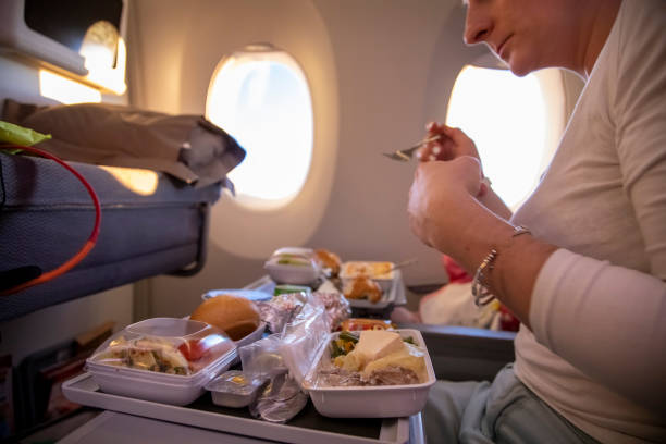 women passenger of aircraft seats in seat and  eats tasty hot inflight meal  on a folding table. in the background is a window in the porthole. side view stock photo