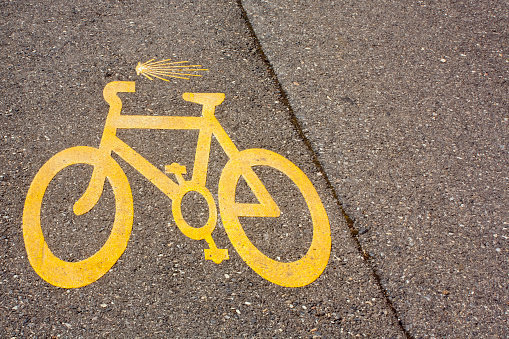 Yellow bicycle and scallop symbols on asphalt road, directional signs in the Camino de Santiago pilgrimage route, Galicia, Spain. Copy space on the right.