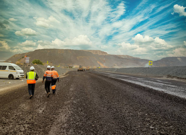 Few African workers walking on a dirt road Few African workers walking on a dirt road at open pit diamond mine, heavy machinery in the background miner stock pictures, royalty-free photos & images