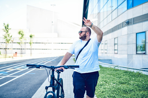 Balding Male Pushing Bicycle And Greeting Other People Outside