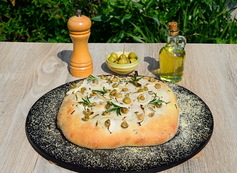 Homemade Italian rosemary, green olive and onion Focaccia bread on a baking stone, England, UK, Europe.