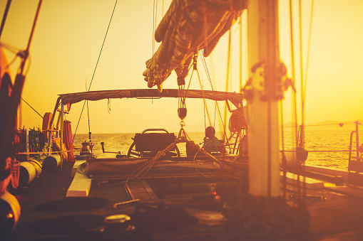 Sailor steering sailing boat with a rudder in dawn / twilight time on tje open sea.