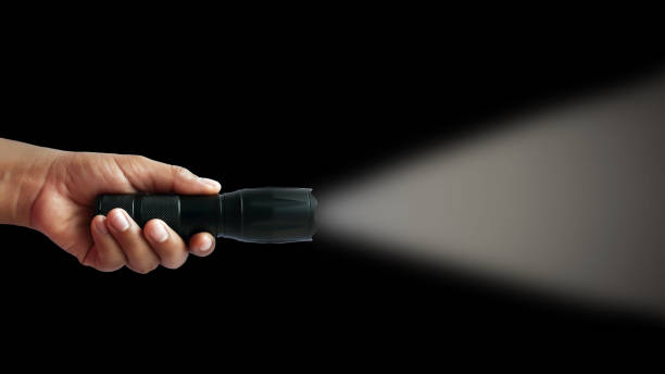 istock Black flashlight in human hands on a black background, including a white beam. 1241323290