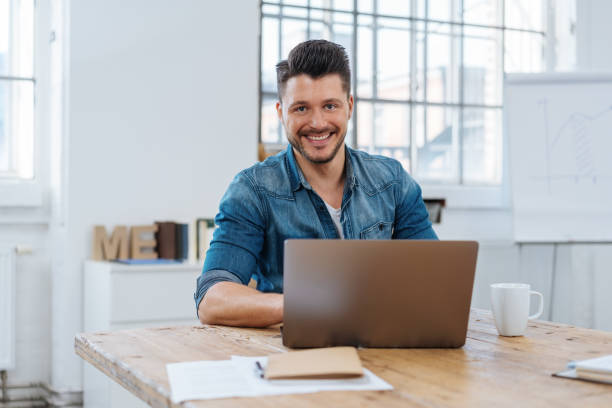 istock Young smiling man sitting in front of laptop 1241329665