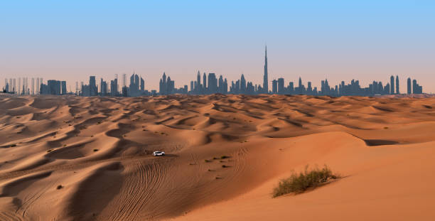 Dubai skyline and desert landscape. Dubai skyline on the horizon of a sand and dune landscape with tire tracks from a 4x4 vehicle during safari excursion. Blue sky at sunset. dubai skyline stock pictures, royalty-free photos & images