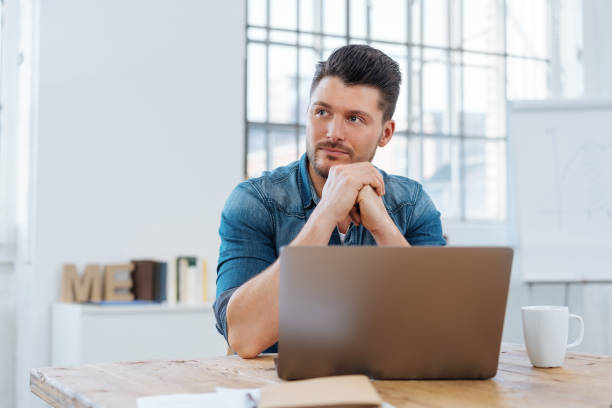 istock Young thoughtful man sitting in front of laptop 1241339452