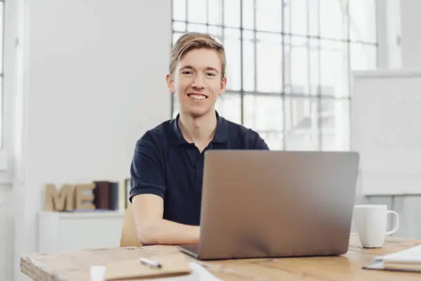 Portrait of young smiling man sitting at table in front of computer