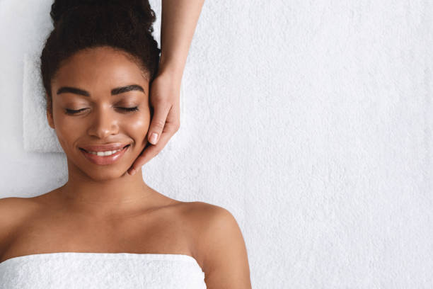 Joyful african girl having face massage at spa Joyful african girl with closed eyes having face massage at spa, top view, copy space black skin stock pictures, royalty-free photos & images