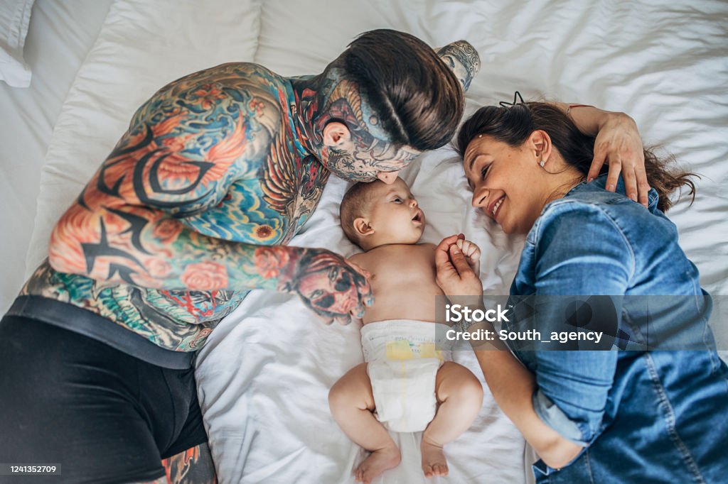 Mother And Father With Whole Body In Covered In Tattoos Lying With His Baby  Son On Bed In Bedroom Stock Photo - Download Image Now - iStock