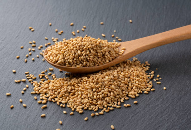 White sesame seeds in a spoon placed on a black background