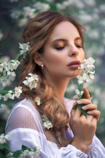 tender portrait of a young beautiful girl with jasmine flowers close-up portrait of a young woman with white flowers in her hands. Soft light. beautiful hairstyle in greek steel, makeup floral crown photos stock pictures, royalty-free photos & images