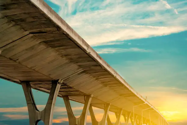 Bottom view of elevated concrete highway. Overpass concrete road. Road flyover structure. Modern motorway with golden sunrise sky. Concrete bridge engineering construction. Bridge architecture.