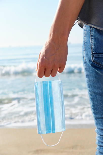 istock man with a surgical mask in his hand on the beach 1241413504