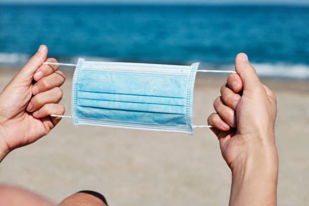 istock man with a surgical mask in his hands on the beach 1241413532