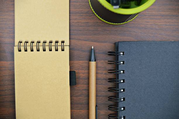 istock Two spiral bound notepad, one open and the other closed with a pen, over a brown table top 1241416234