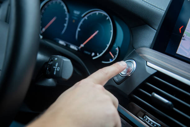 male finger presses the start stop engine button on a car dashboard. close-up, soft focus, in the background the dashboard and car speedometer in blur, side view stock photo